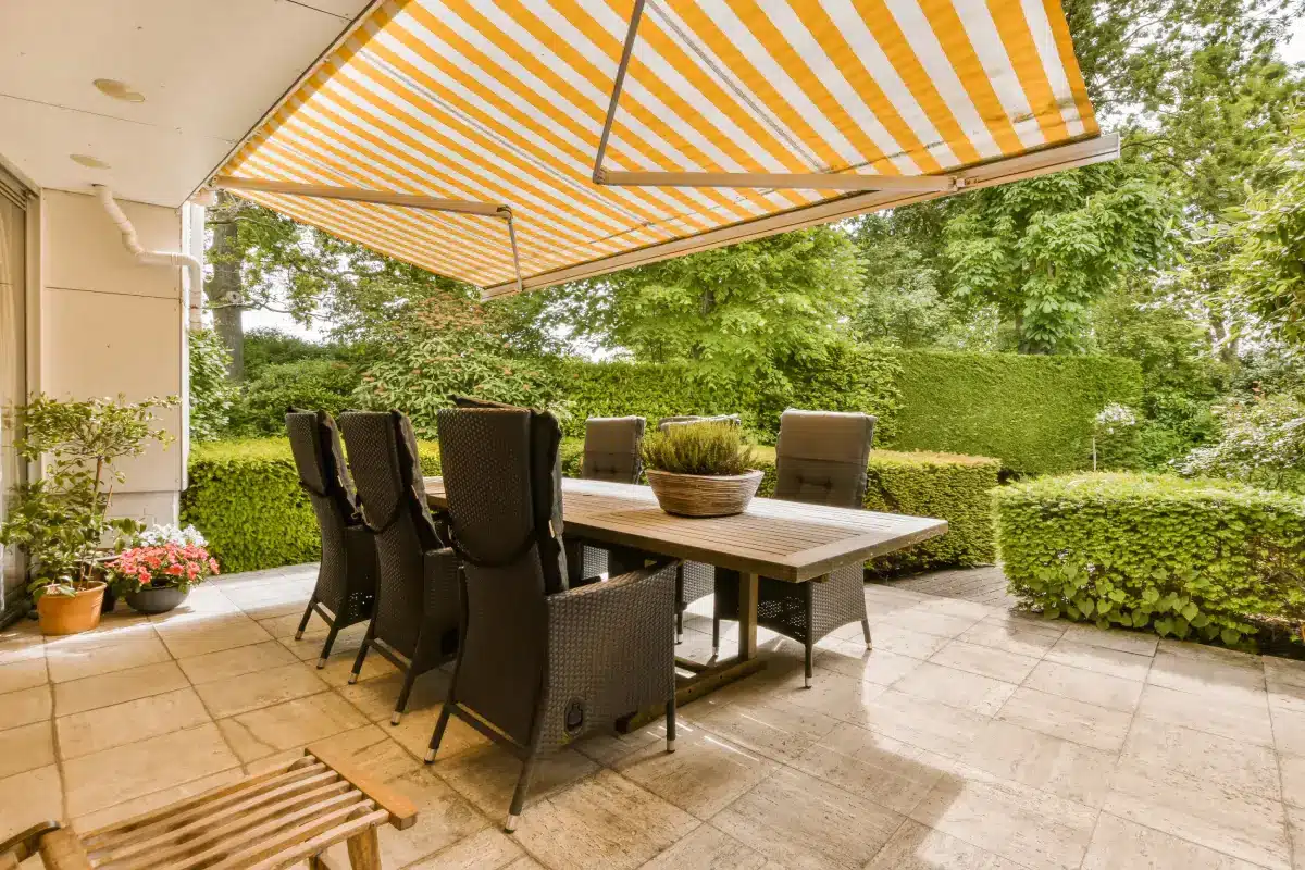Yellow and white striped retractable awning shading a patio dining set.